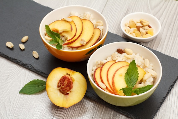 Gachas de sorgo con melocotón, anacardos, almendra y hojas de menta en cuencos de porcelana sobre tablero de piedra. Ensalada vegana de sorgo sin gluten con frutas frescas. Vista superior.