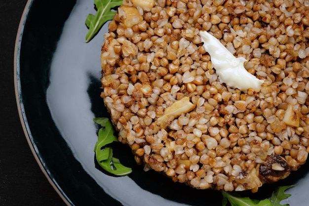 Gachas de trigo sarraceno con mantequilla y hierbas en un plato sobre un fondo oscuro