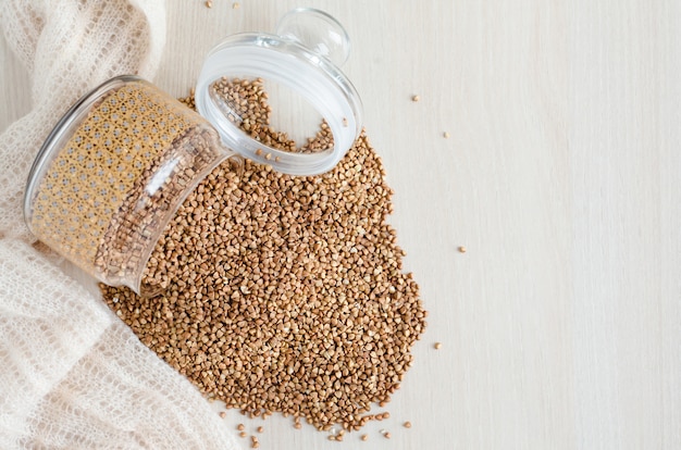 Gachas de trigo sarraceno stock en frasco de vidrio sobre fondo blanco de madera, espacio de copia. Comida sana y nutritiva en crisis y hambre.