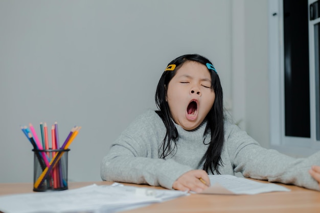 Gähnendes asiatisches Mädchen beim Arbeiten an einem Schreibtisch