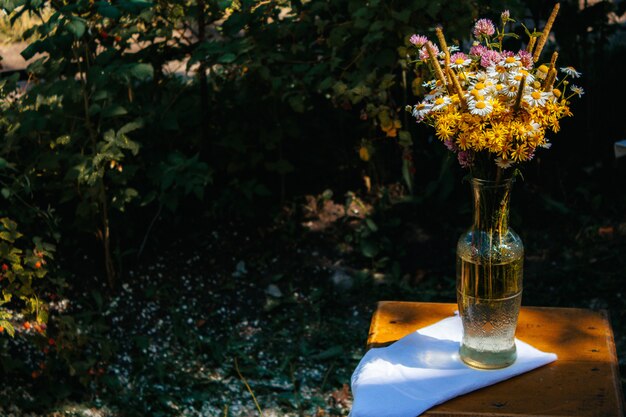 Gänseblümchen, Klee, gelbe Blumen, Gras Segge in einem Feldstrauß sind in einer Vase im Garten auf einem Stuhl