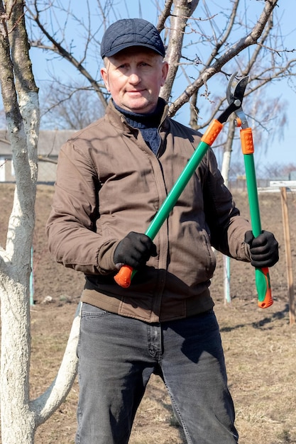 Gärtner im Garten in der Nähe der Bäume mit großen Gartenscheren