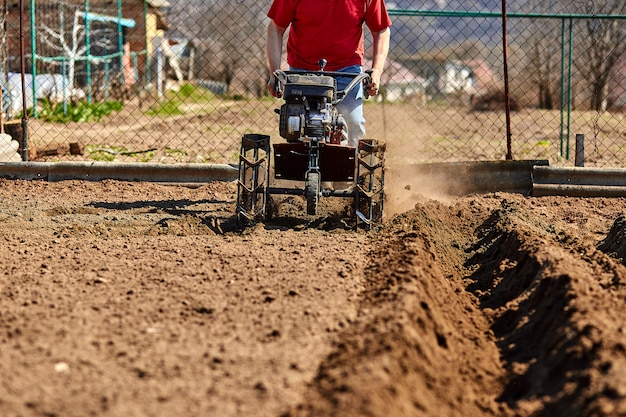 Gärtner Mann kultivieren Boden mit Pinne Traktor oder Rototiller, Cutivator, Miiling Maschine, bereiten für das Pflanzen der Ernte im Frühjahr.