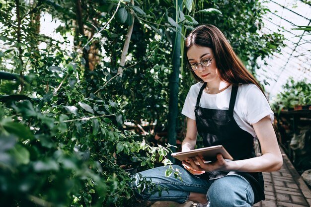 Gärtnerin der jungen Frau mit digitaler Tablette, die im Gewächshaus arbeitet