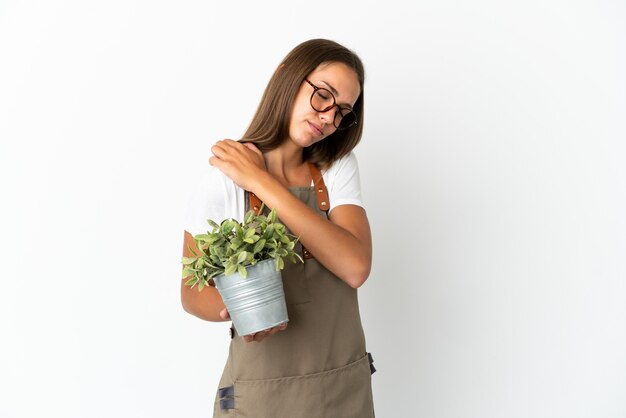 Gärtnermädchen, das eine Pflanze über lokalisiertem weißem Hintergrund hält, der unter Schmerzen in der Schulter leidet, weil sie sich bemüht haben