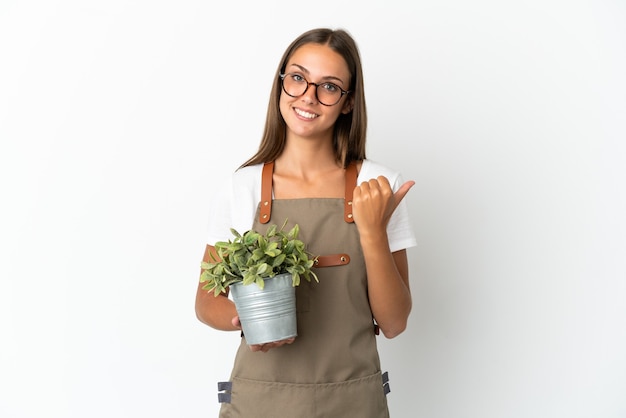 Gärtnermädchen, das eine Pflanze über lokalisiertem weißem Hintergrund hält, der zur Seite zeigt, um ein Produkt zu präsentieren