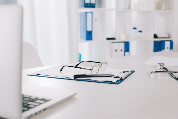 Foto gafas y bolígrafo en el portapapeles en la mesa de trabajo en la clínica