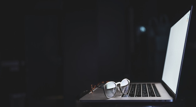 Las gafas se encuentran en la computadora portátil, reflejando la luz de la pantalla en la oscuridad, copie el espacio.