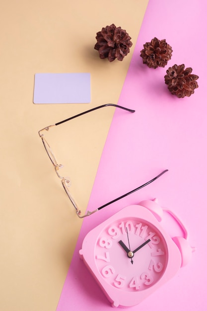 Gafas con estilo sobre fondo pastel. Tarjeta de visita, colores pastel rosa y amarillo. Reloj despertador, flores de abeto.