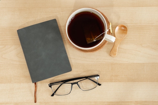 Gafas de lectura de cuaderno gris y taza de té en el escritorio de oficina de madera