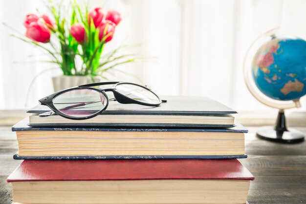 Gafas de lectura poner libros de tapa dura sobre una mesa de madera junto a la ventana