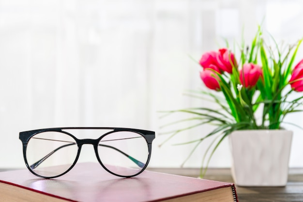 Gafas de lectura poner libros de tapa dura sobre una mesa de madera junto a la ventana