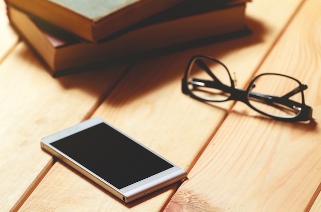 Gafas, libros y teléfono móvil en una mesa de madera