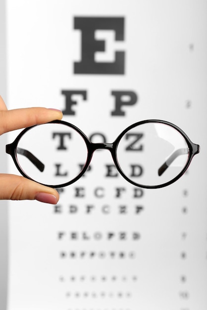 Foto gafas en las manos en primer plano de fondo de tabla optométrica