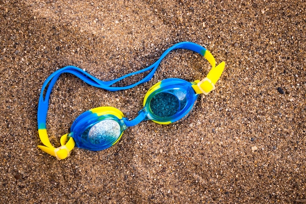 Gafas de natación azules para niños en las vacaciones de arena con concepto de horario de verano para niños