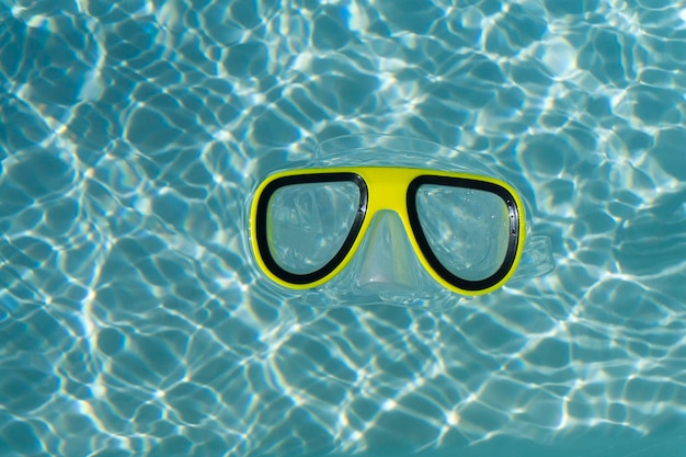Unas gafas de natación de esnórquel amarillas flotando en una piscina ondulada de color azul claro