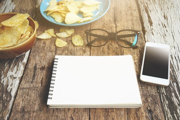 Gafas y patatas fritas del smartphone del cuaderno en el escritorio