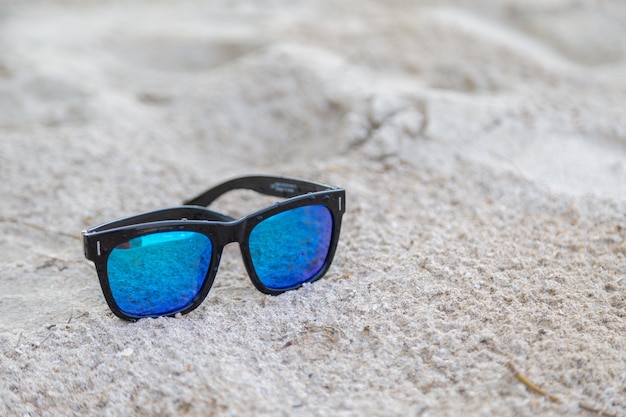 Gafas de sol azules sobre fondo de arena blanca