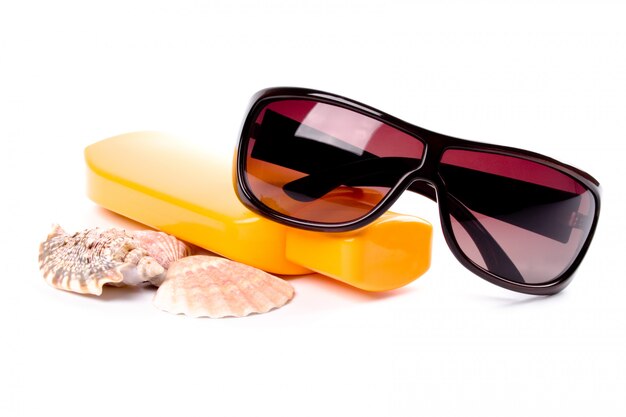 Gafas de sol, conchas y loción closeup sobre fondo blanco