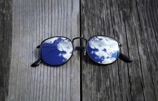 Gafas de sol espejadas de cerca en el muelle de madera con nubes y reflejo del cielo