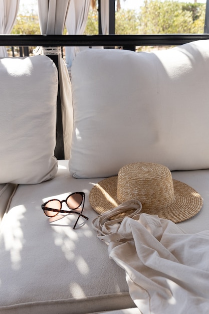 Gafas de sol femeninas con estilo, sombrero de paja, bolso de compras en el sofá blanco con almohadas.