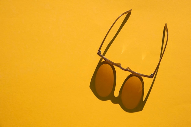 Gafas de sol con una larga sombra sobre un fondo amarillo brillante de verano