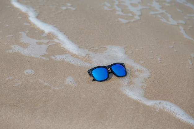 Gafas de sol de moda azul en la arena con fondo de onda y playa