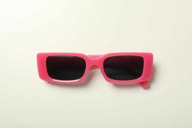 Gafas de sol oscuras con un marco rosado sobre un fondo claro
