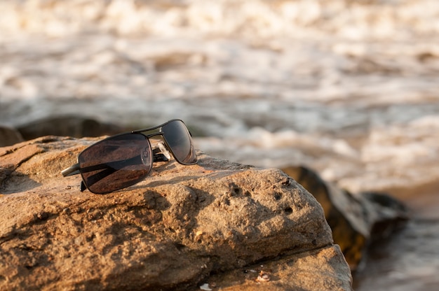 Gafas de sol oscuras sobre una piedra sobre un fondo borroso del mar