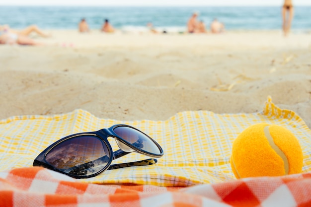 Foto gafas de sol y una pelota de tenis sobre una manta en el fondo de la playa en verano