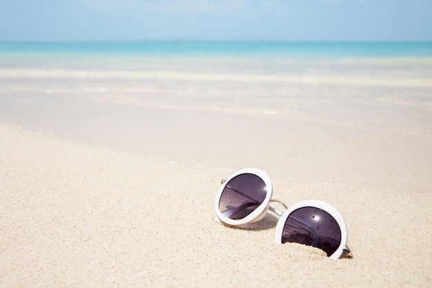 Gafas de sol en la playa de arena de mar azul en verano