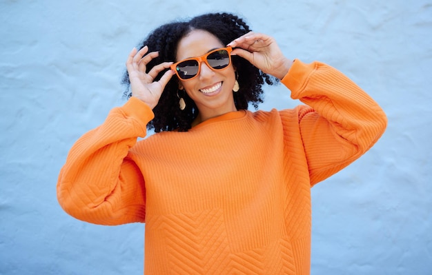 Gafas de sol de retrato de moda y mujer negra aislada sobre fondo azul gen z juventud o ropa de moda Persona feliz o modelo de belleza en estilo de visión de confianza y color naranja en maqueta de pared de ladrillo