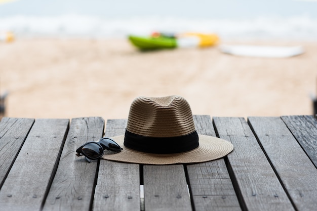 Foto gafas de sol y sombrero de paja en el piso de madera en la playa, concepto del verano.