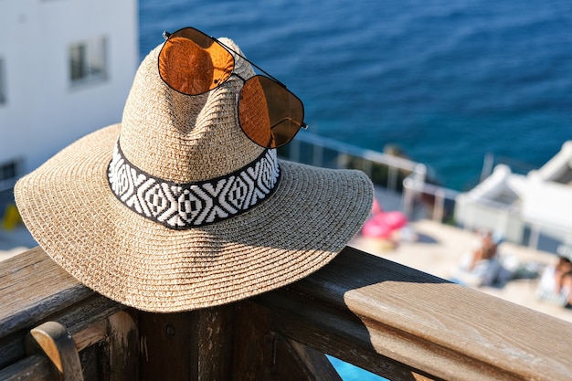 Gafas de sol de sombrero de paja en la terraza de madera con vistas al mar y a la piscina