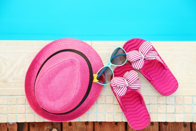 Gafas de sol con sombrero rosa y chanclas junto a la piscina