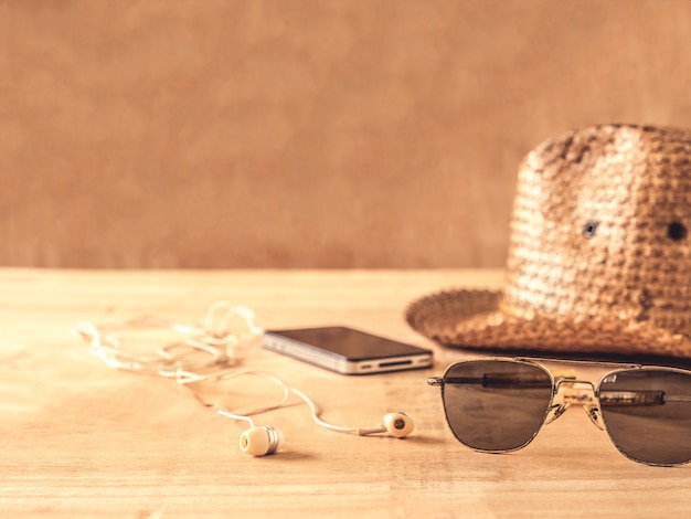 Gafas de sol, sombrero, teléfono inteligente y auriculares en la mesa de madera