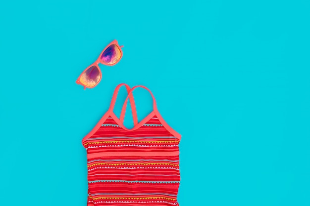 Gafas de sol y traje de baño, un conjunto brillante para una niña para unas vacaciones de playa en colores de moda sobre un fondo azul.