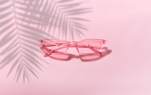 Gafas de sol de verano sobre un fondo rosa con sombra de palmera