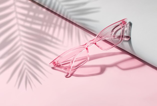 Gafas de sol de verano sobre un fondo rosa con sombra de palmera