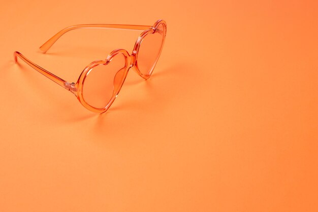 Las gafas de sol de verano yacen sobre el cabello rosado en la pared naranja. Copie el espacio.