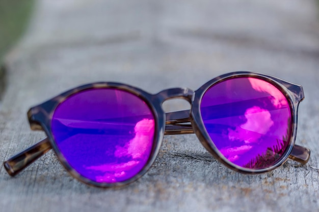 Las gafas de sol yacen sobre una vieja mesa de madera que reflejan el cielo y las nubes