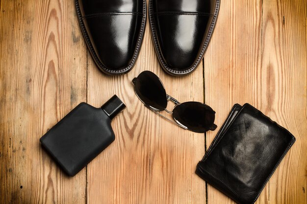 Gafas de sol de zapatos negros y una billetera en una mesa de madera