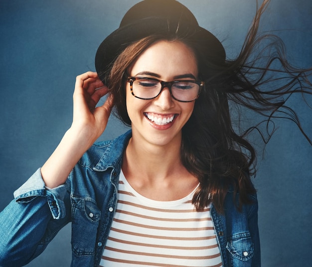 Gafas sonrisa y gen z chica en el estudio con confianza de viento y fedora en fondo oscuro mujer felicidad y moda con gafas para la visión lentes de cuidado de ojos y nuevo marco con accesorios