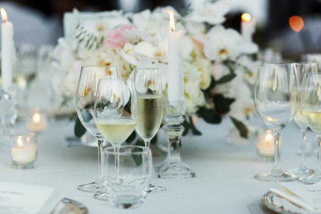 Gafas con vino blanco y champán están parados alrededor del ramo blanco en la mesa