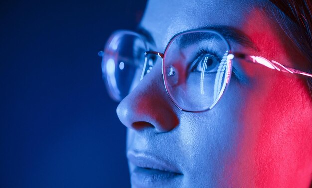 En gafas Vista de cerca Mujer hermosa joven está adentro en el estudio iluminado por luz de neón