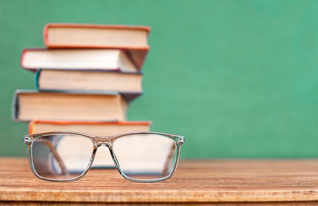 las gafas yacen sobre la mesa contra el fondo de una pila de libros y una pizarra