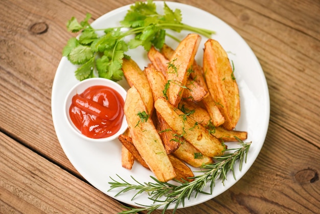 Gajos de patata en un plato blanco con cilantro de hierbas de romero y salsa de tomate ketchup Cocinar patatas fritas o patatas fritas