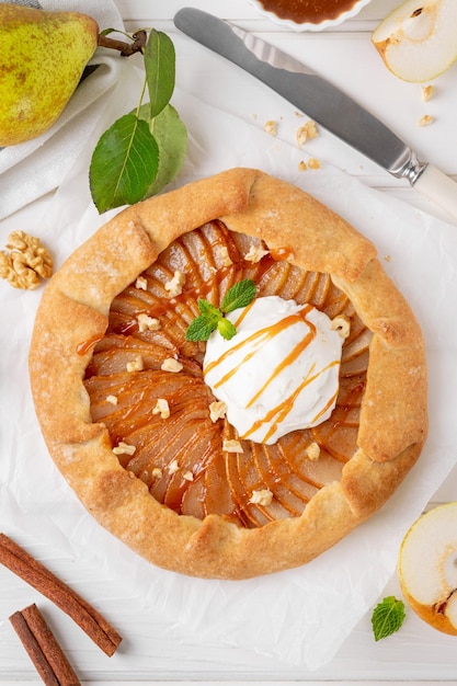 Galeta de otoño con helado de peras, nueces, salsa de caramelo y canela sobre un fondo blanco de madera