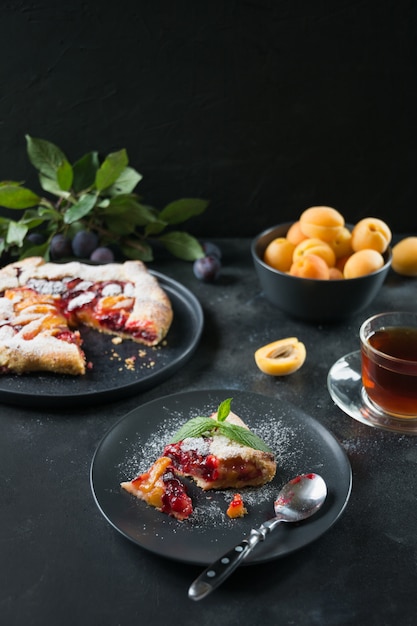 Galette de torta saborosa queda com ameixa e damasco na mesa preta.