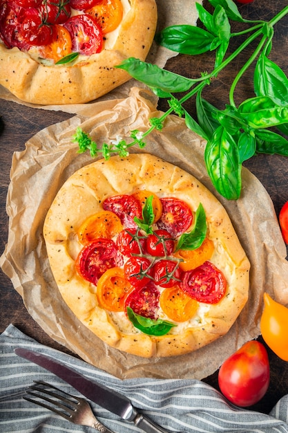 Foto galettes caseros frescos con tomates, queso ricotta y albahaca sobre fondo de madera contrachapada rústica